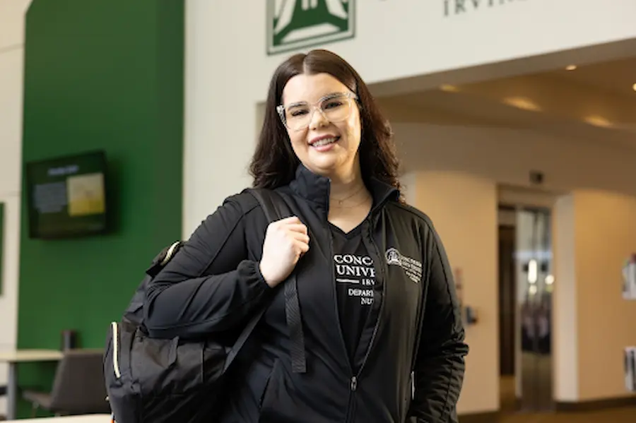 A woman with glasses, smiling and holding a backpack 